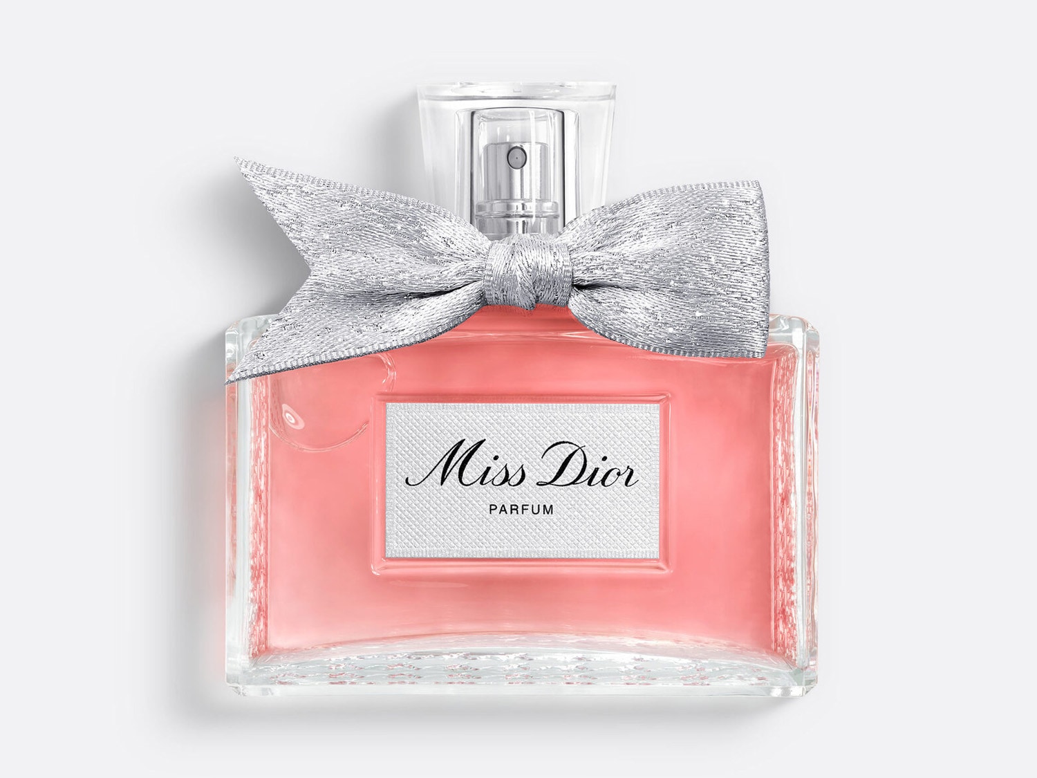 El frasco de perfume Miss Dior presenta un lazo plateado brillante y está lleno de una fragancia rosa pálido, con la marca "Miss Dior PARFUM" en una etiqueta blanca.
