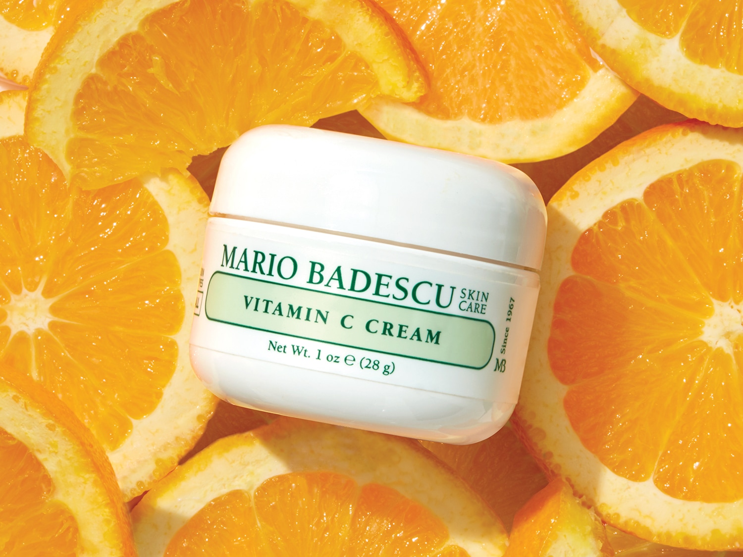 Een potje Mario Badescu vitamine C crème, omringd door verse sinaasappelschijfjes, belooft een heldere en stralende huid.
