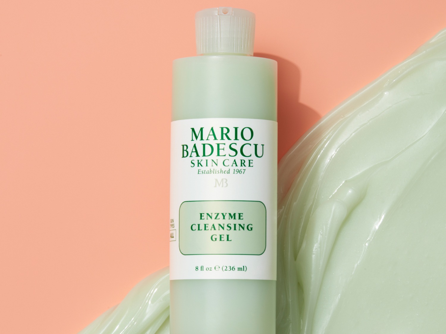 Een lichtgroene fles Mario Badescu Enzyme Cleansing Gel staat naast een klodder van dezelfde gel, klaar om je huid te reinigen.