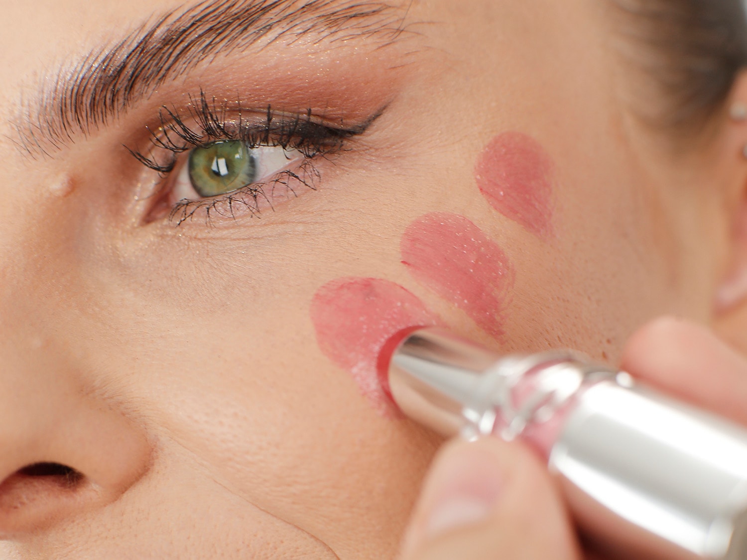 Nahaufnahme eines Gesichts, auf das mit einem silbernen Lippenstift rosa Farbe aufgetragen wird, um die Farbe des Produkts zu demonstrieren.