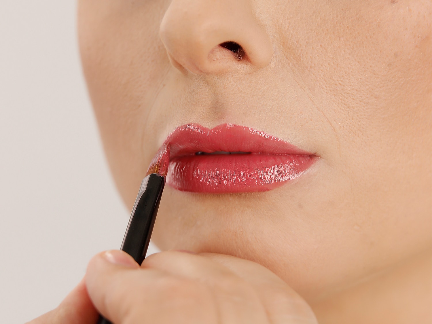 Nahaufnahme einer Person, die mit einem Pinsel einen glänzenden, rosafarbenen Lippenstift aufträgt, um einen strahlenden Look zu erzielen.