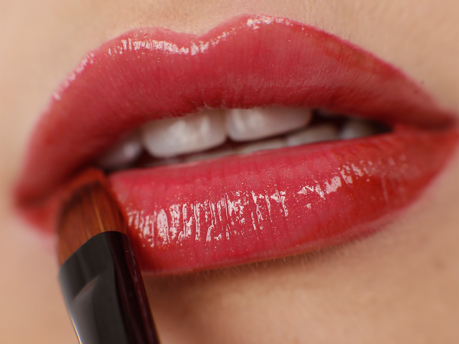 Nahaufnahme von glänzenden, roten Lippen, auf die mit einem Pinsel Lippenstift aufgetragen wird, um einen vollen, sinnlichen Look zu erzielen.