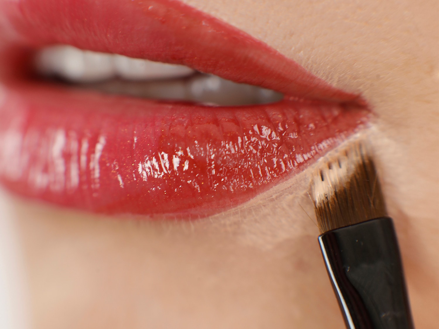 Nahaufnahme von glänzenden, roten Lippen, auf die mit einem Pinsel Lippenstift aufgetragen wird, um einen präzisen und vollen Look zu erzielen.