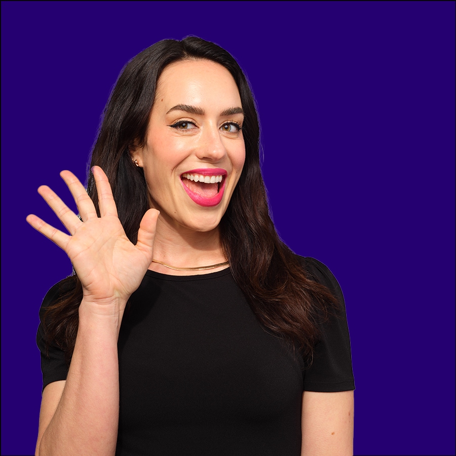 Eine strahlende Frau mit dunklen Haaren und pinkfarbenem Lippenstift lächelt und winkt vor einem violetten Hintergrund.