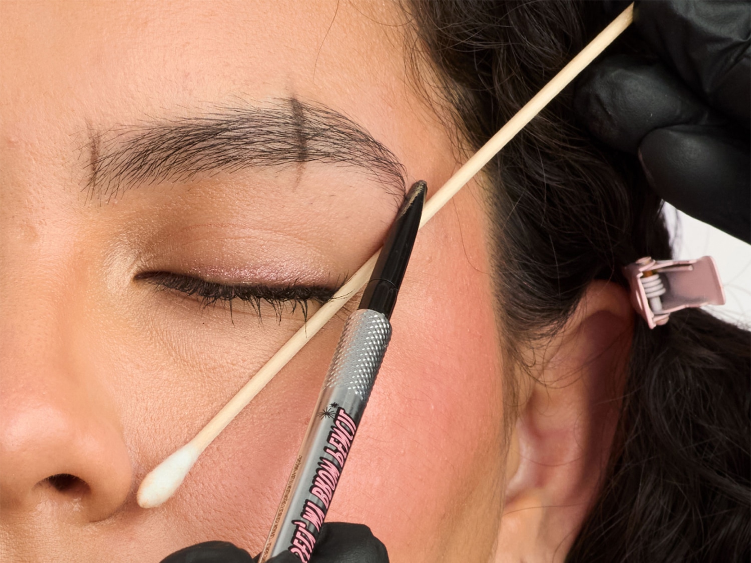 Nahaufnahme einer Frau, die mit einem Wattestäbchen und einem Augenbrauenstift ihre Augenbrauen formt, um einen präzisen Look zu erzielen.