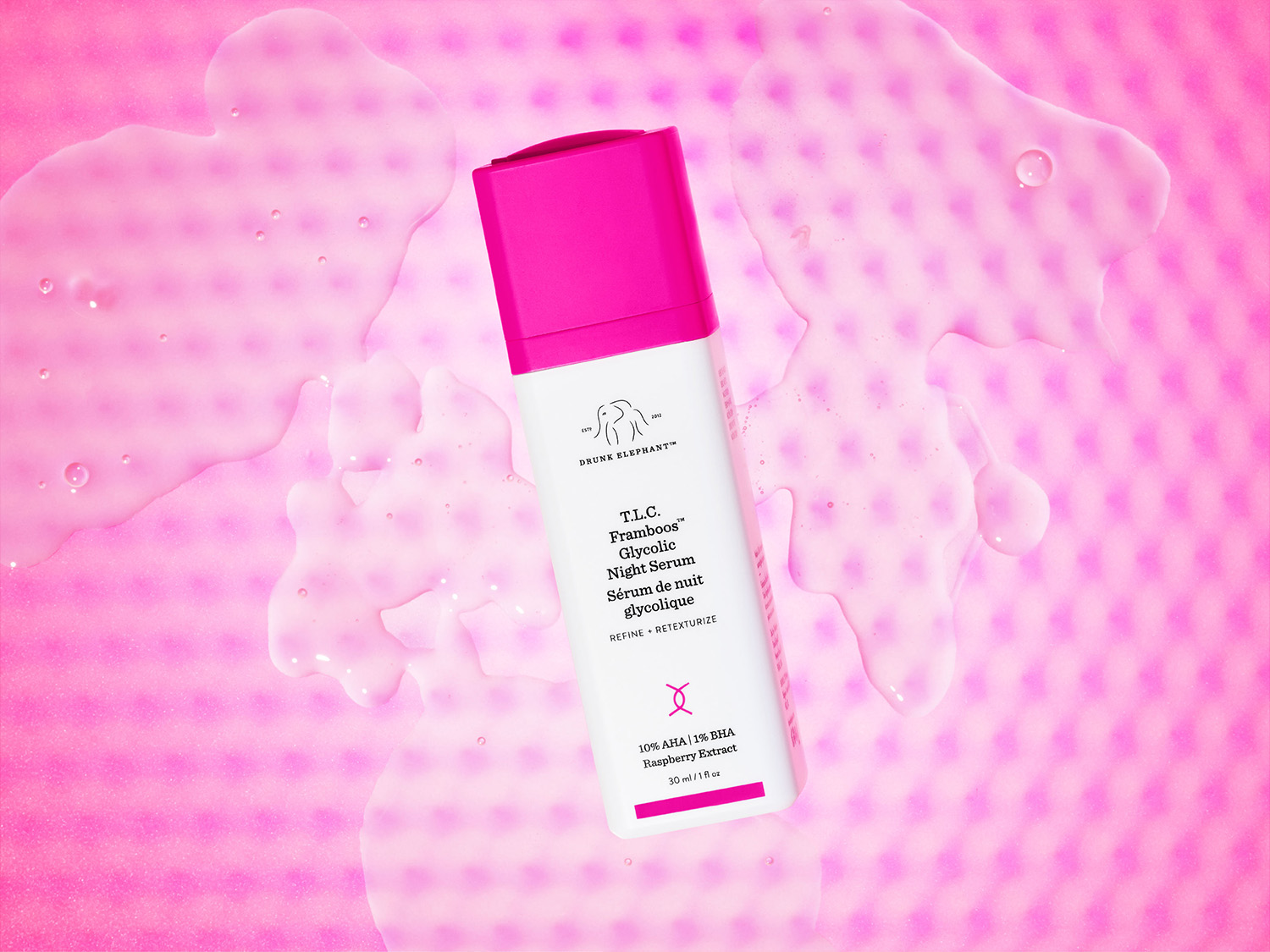 Auf einem rosa Hintergrund mit transparenten Gel-Akzenten präsentiert sich eine weiße Flasche Drunk Elephant T.L.C. Framboos™ Glycolic Night Serum mit einem leuchtend pinkfarbenen Verschluss.