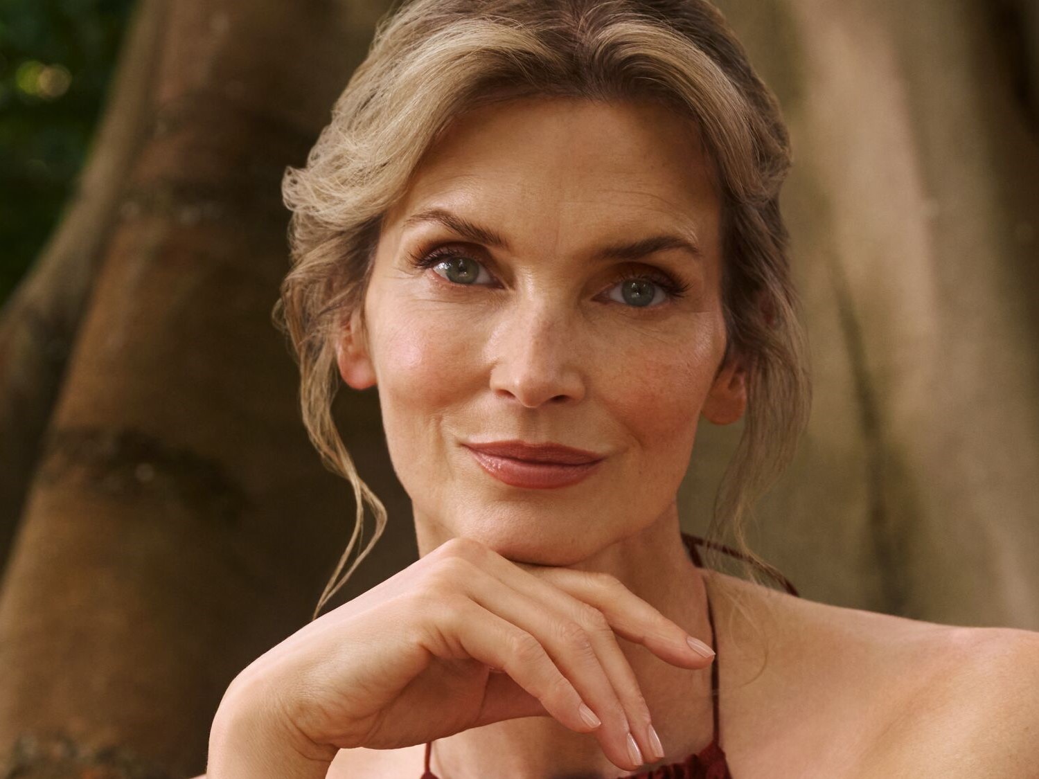 Porträt einer Frau mit blondem Haar und einem natürlichen Make-up, die ihre Hand unter ihr Kinn legt und einen nachdenklichen Ausdruck zeigt.