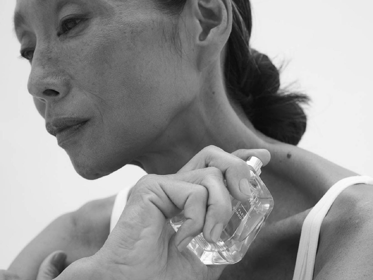 Eine Frau sprüht sich Parfüm aus einer transparenten Flasche mit silbernem Verschluss auf den Hals.