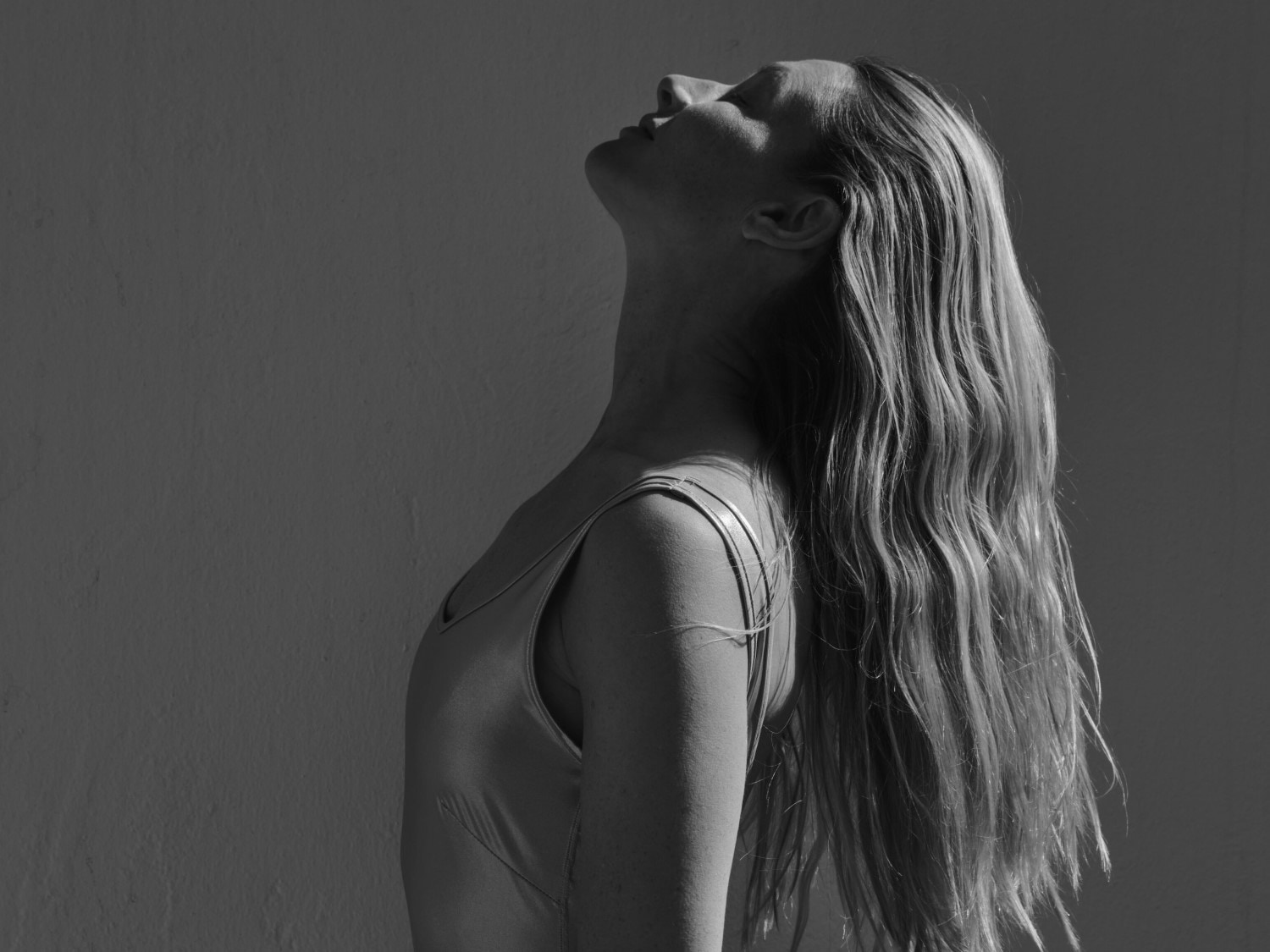 Eine Frau mit langen, gewellten Haaren und einem glänzenden Oberteil blickt mit zurückgelehntem Kopf in Richtung des Himmels.