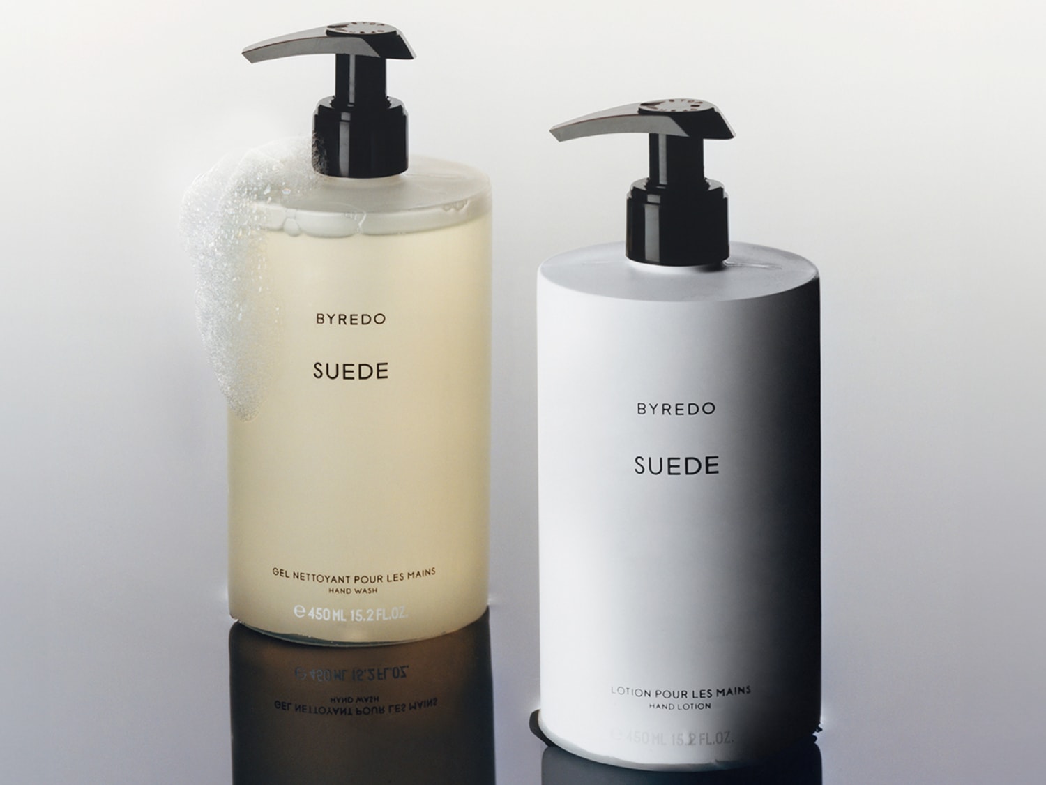 Dva produkty péče o ruce Byredo Suede: průhledná láhev s pumpičkou s mycím gelem a bílá láhev s pumpičkou s pleťovou vodou.