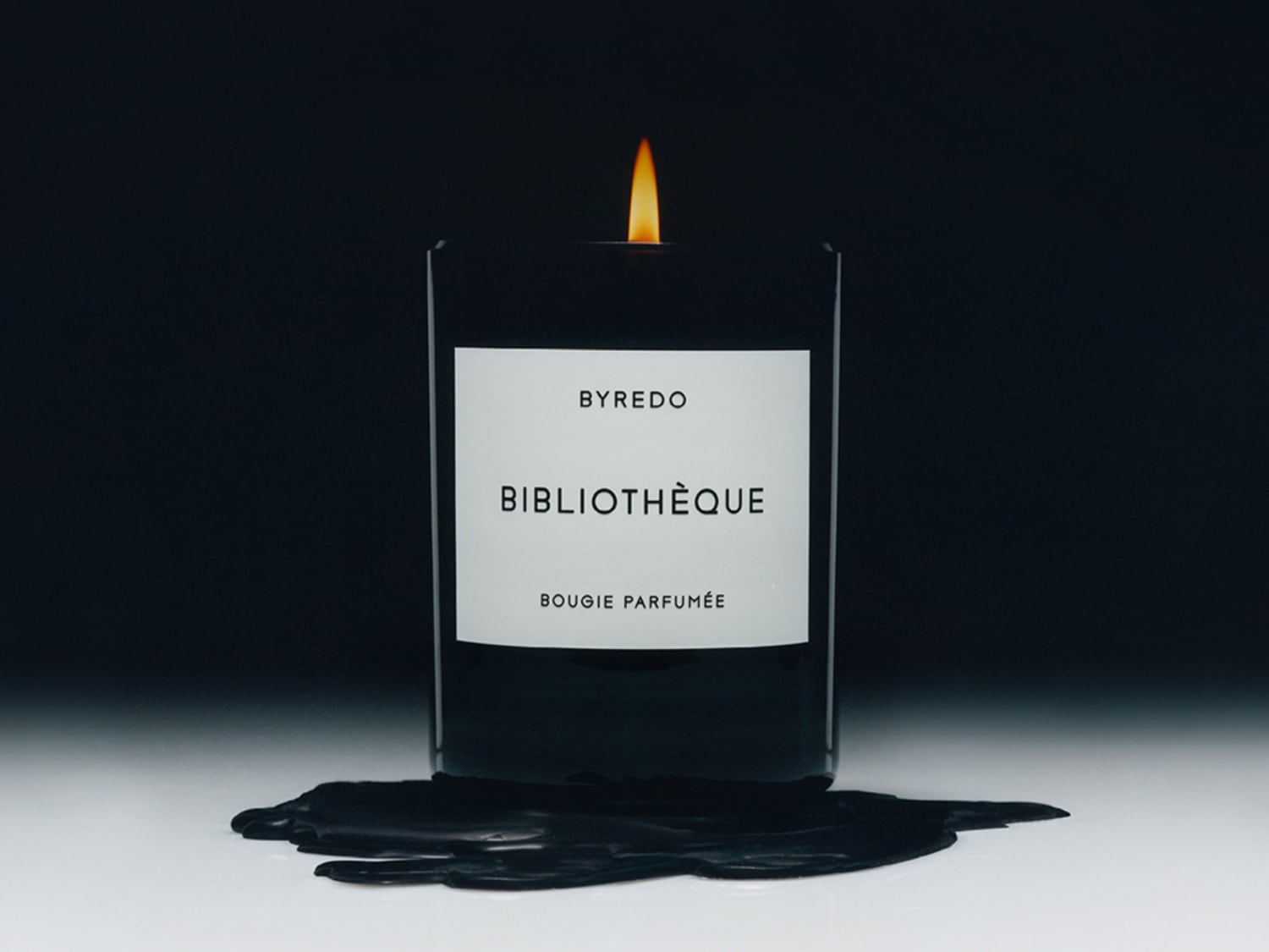 Černá svíčka Byredo Bibliothèque Bougie Parfumée s hořícím plamenem a rozlitým voskem vytváří útulnou atmosféru.