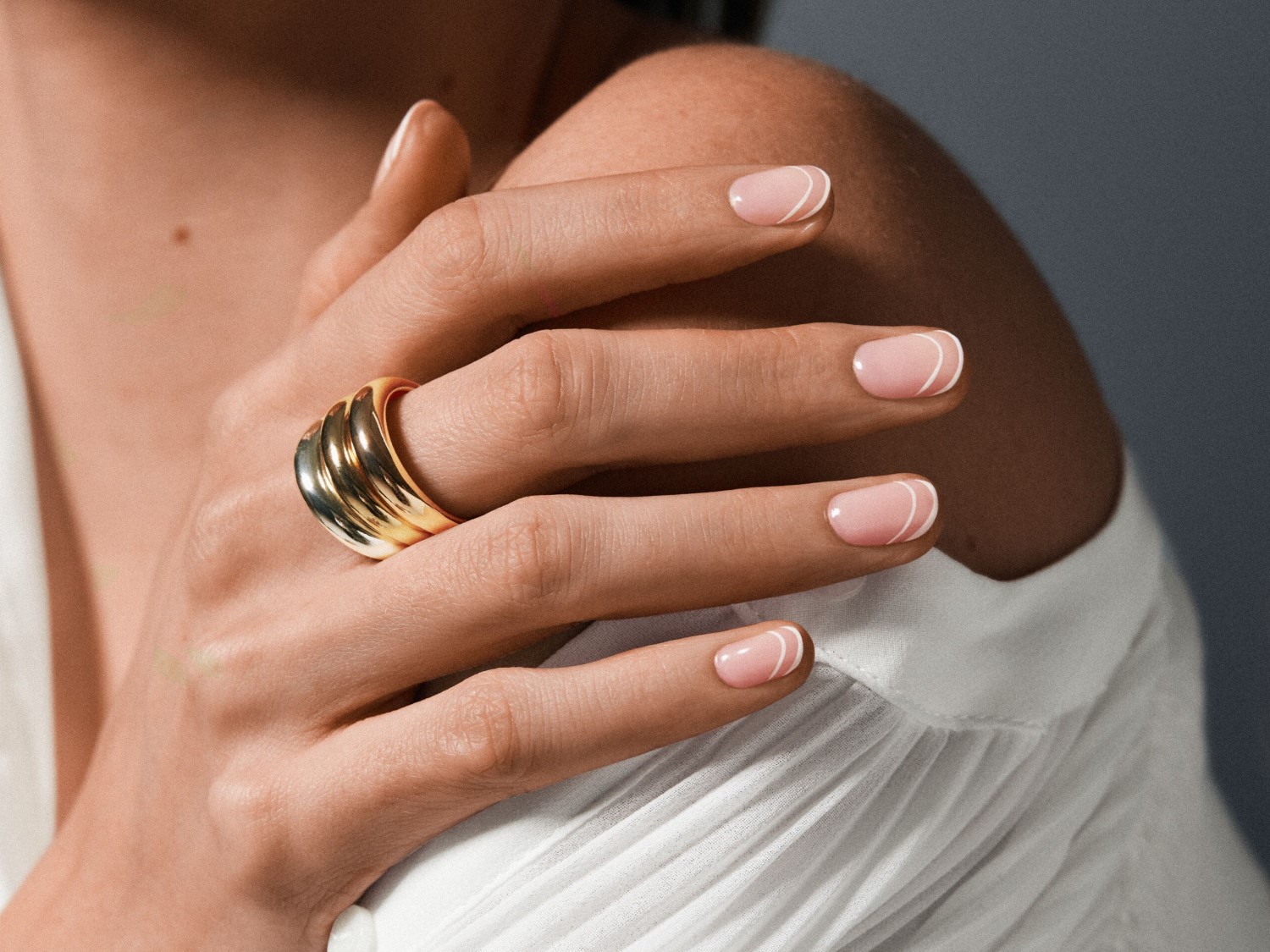 Vrouwenhand met een gouden ring en nagels met een witte halvemaanvormige versiering, tegen een achtergrond van een witte blouse.