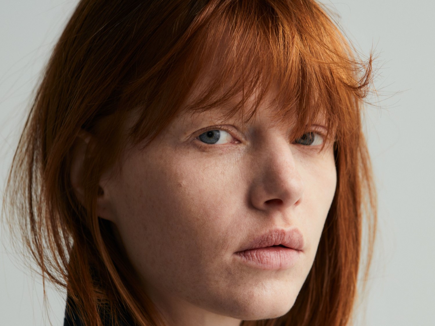 Portret kobiety z rudymi włosami i niebieskimi oczami, skierowanej wprost, z delikatnym makijażem.