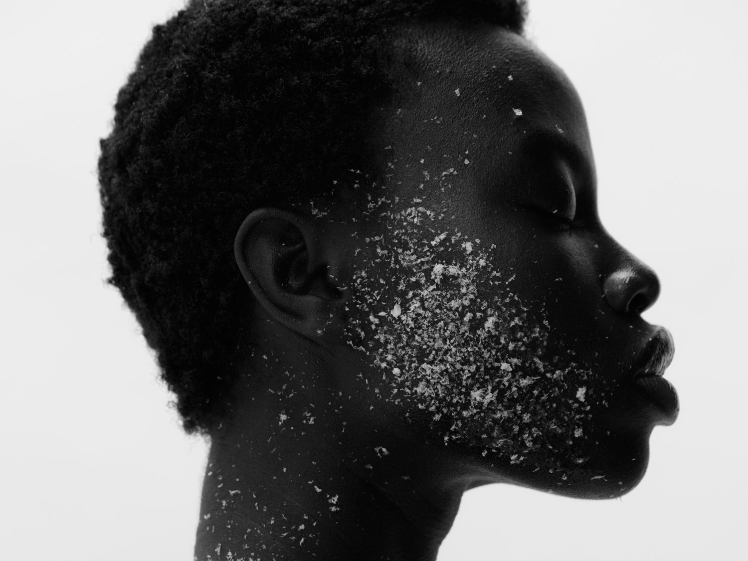 Nahaufnahme eines schwarzen Models mit geschlossenen Augen und weißem Puder auf Gesicht und Hals, das einen monochromen, minimalistischen Beauty-Look erzeugt.