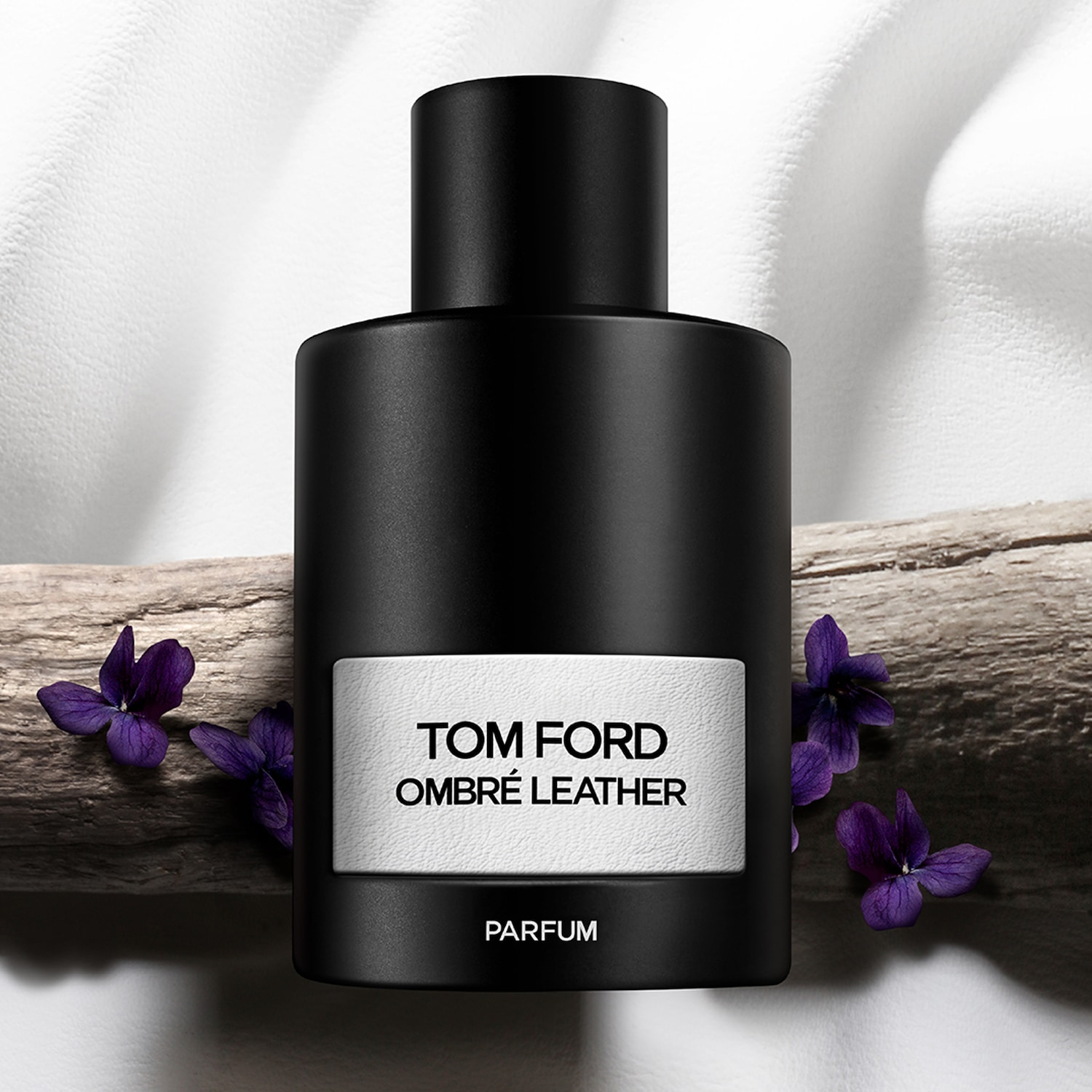 Découvrez le parfum Ombré Leather de Tom Ford, présenté dans un flacon noir élégant, rehaussé de délicates fleurs violettes et d'une touche naturelle de bois.