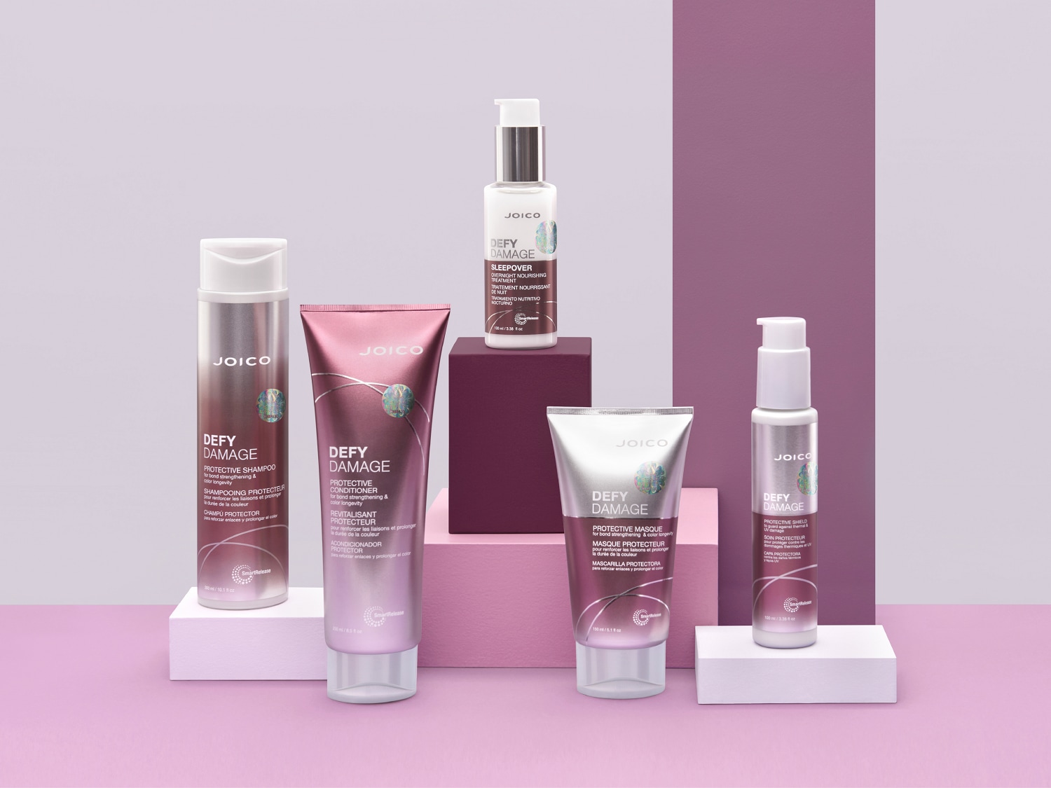 Kolekcja Joico Defy Damage w odcieniach fioletu i srebra, obejmująca szampon, odżywkę, maskę i kurację, które chronią włosy i przedłużają trwałość koloru.