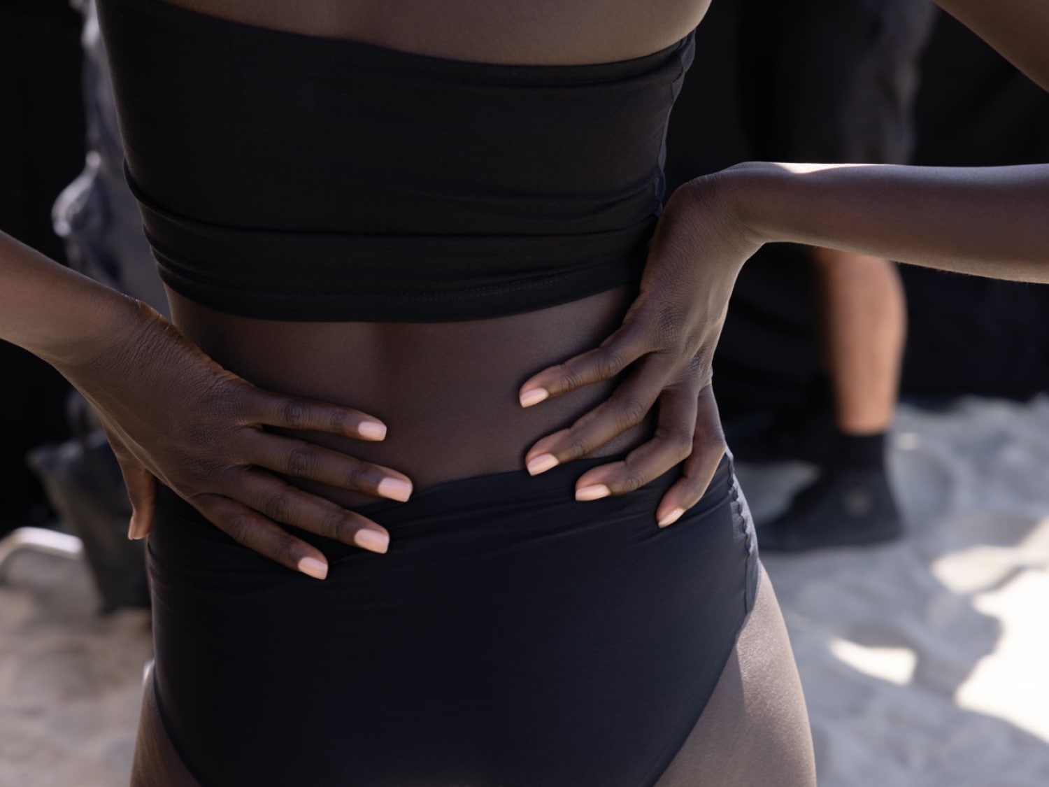 Een vrouw met een donkere huidskleur draagt een zwarte bikini en heeft haar handen in haar zij.