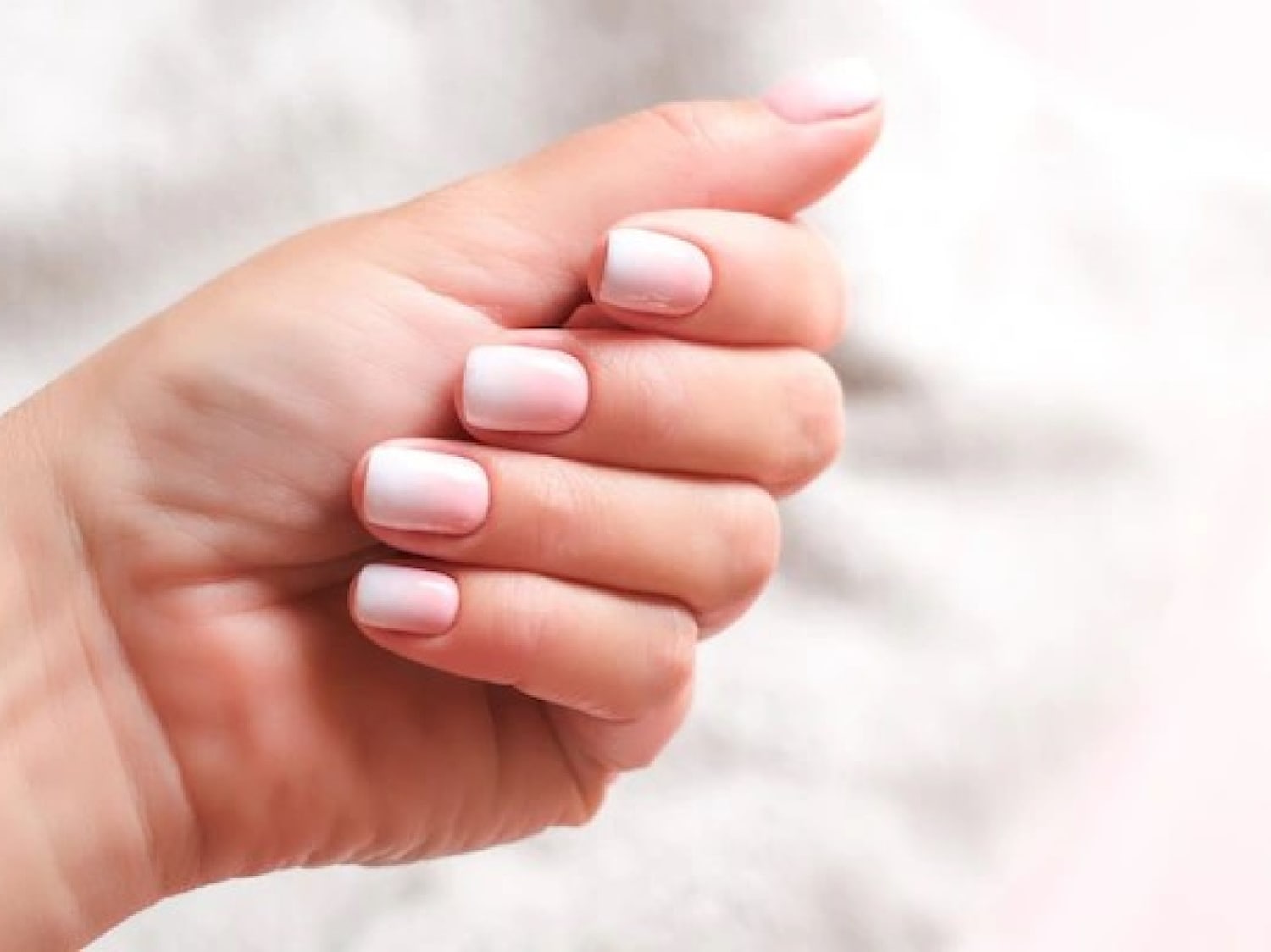 Close-up van een hand met nagels die een zachte, roze-witte ombre-look hebben, perfect voor een subtiele en elegante uitstraling.