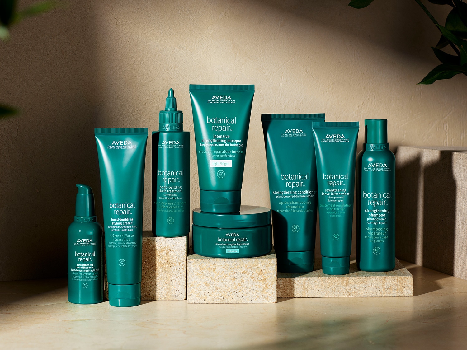 Eine Sammlung von Aveda Botanical Repair-Haarpflegeprodukten in grünen Verpackungen, die auf hellen Blöcken angeordnet sind.