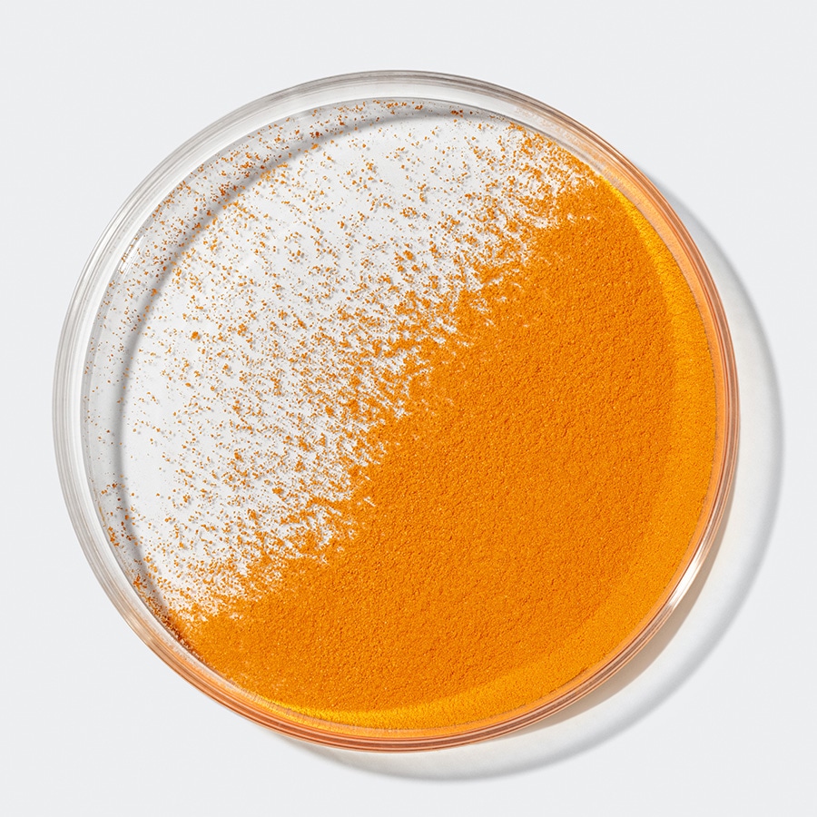 Nahaufnahme einer Petrischale, die teilweise mit einem leuchtend orangefarbenen Pulver gefüllt ist, das sich zum Rand hin ausdünnt.