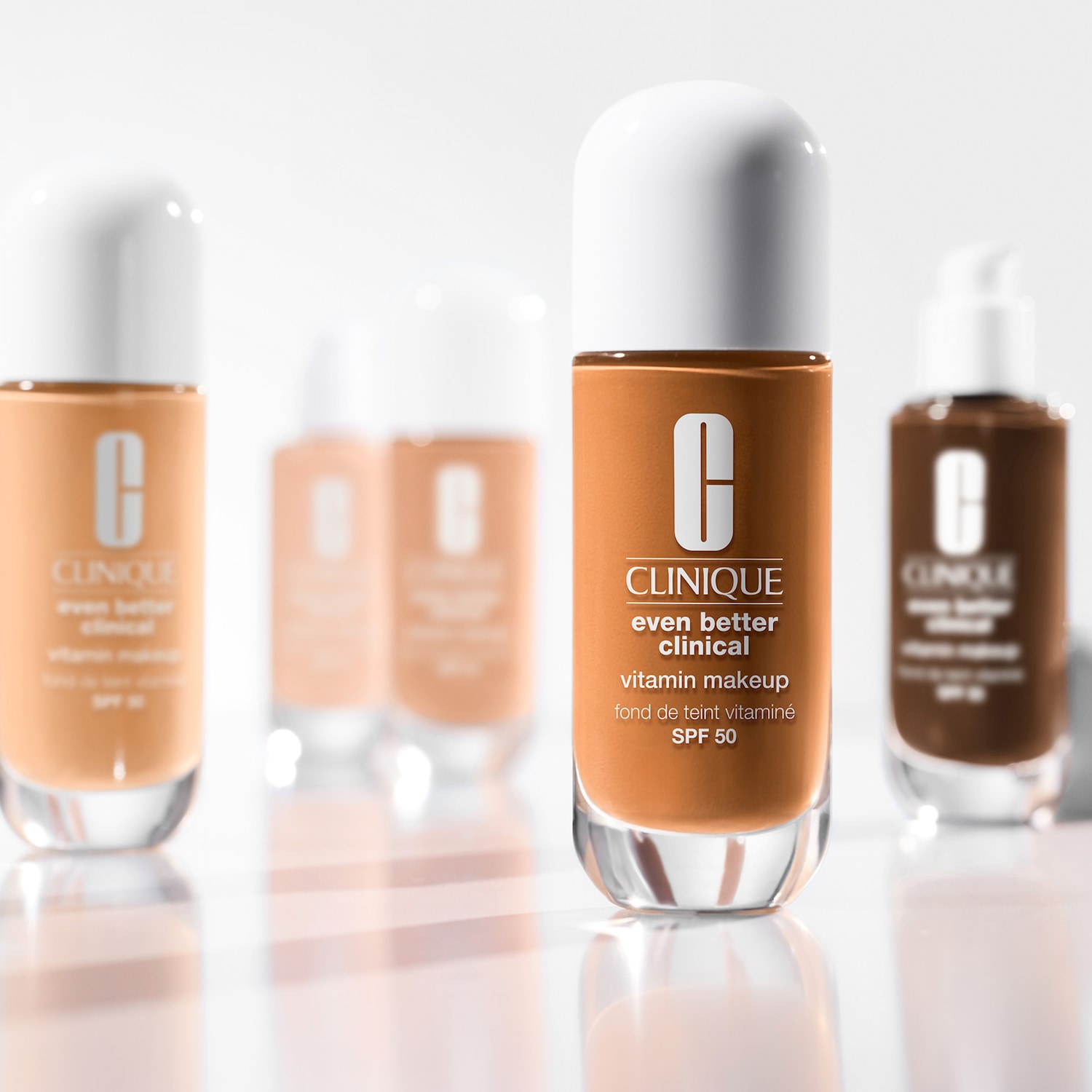Clinique Even Better Clinical Vitamin Makeup mit SPF 50 in verschiedenen Farbtönen, die in klaren Glasflaschen mit weißen Kappen präsentiert werden.