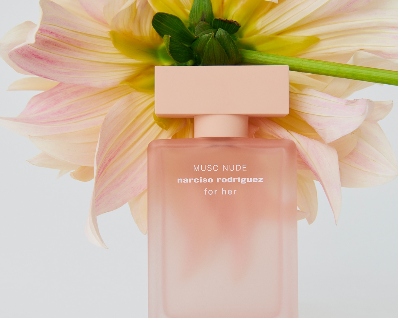 Narciso Rodriguez For Her Musc Nude parfém v bledě růžovém flakonu s květinou v pozadí.