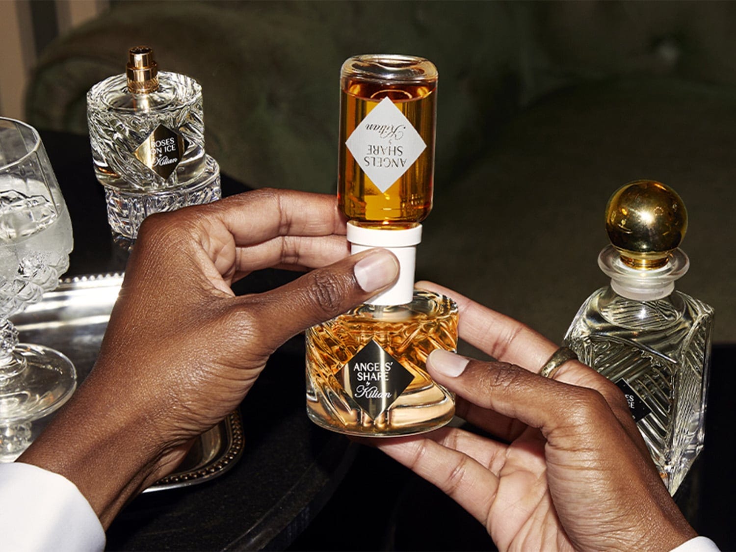 A Kilian Angels' Share parfümöt egy személy tartja, mellette Roses on Ice parfüm látható, elegáns és kifinomult illatélményt kínálva.