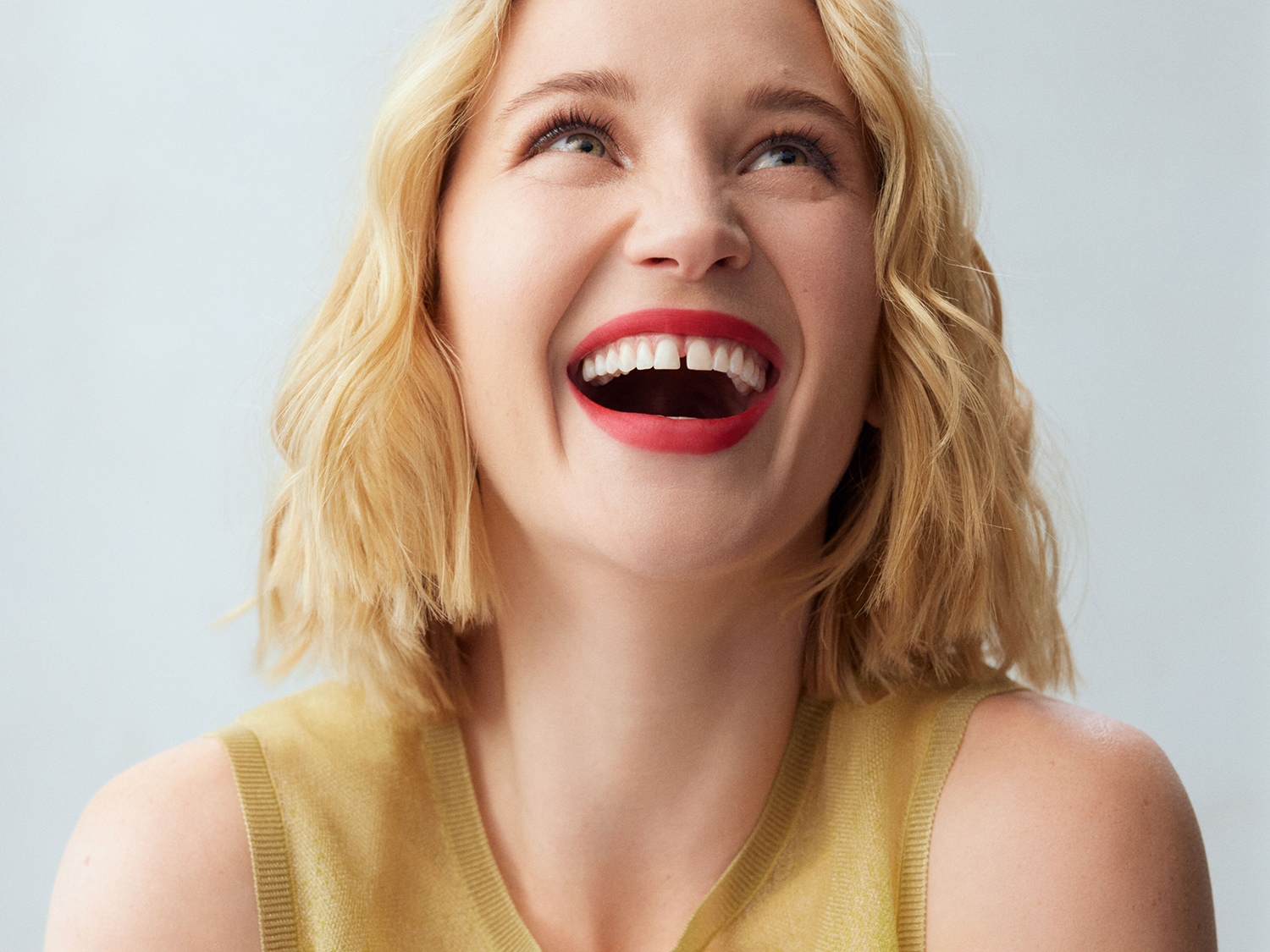 Portrét usmievavej ženy s blond vlasmi a červeným rúžom, ktorá sa pozerá nahor.