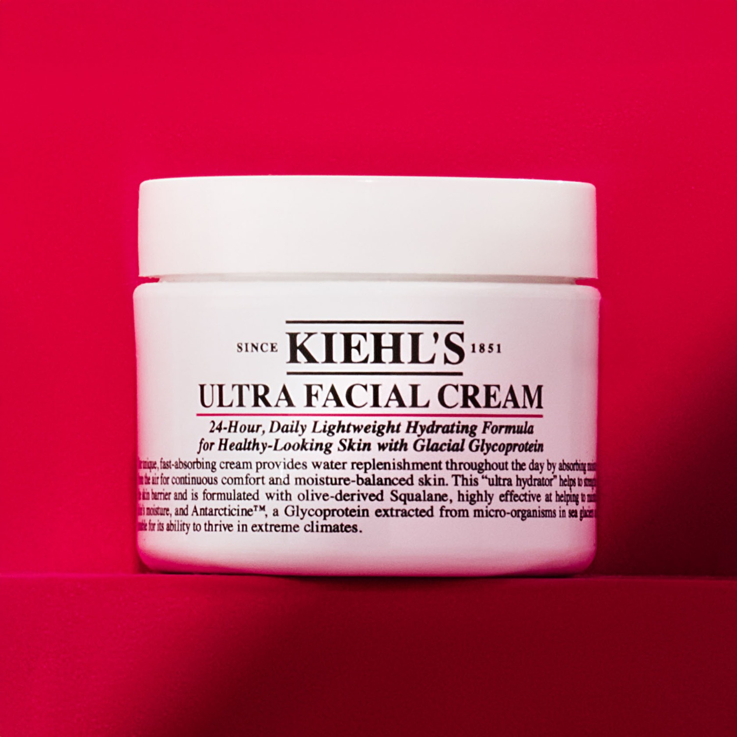 Découvrez la Crème Ultra Faciale de Kiehl's, une formule hydratante légère pour une peau d'apparence saine, enrichie en Glycoprotéine Glaciaire, dans un pot blanc sur fond rouge.