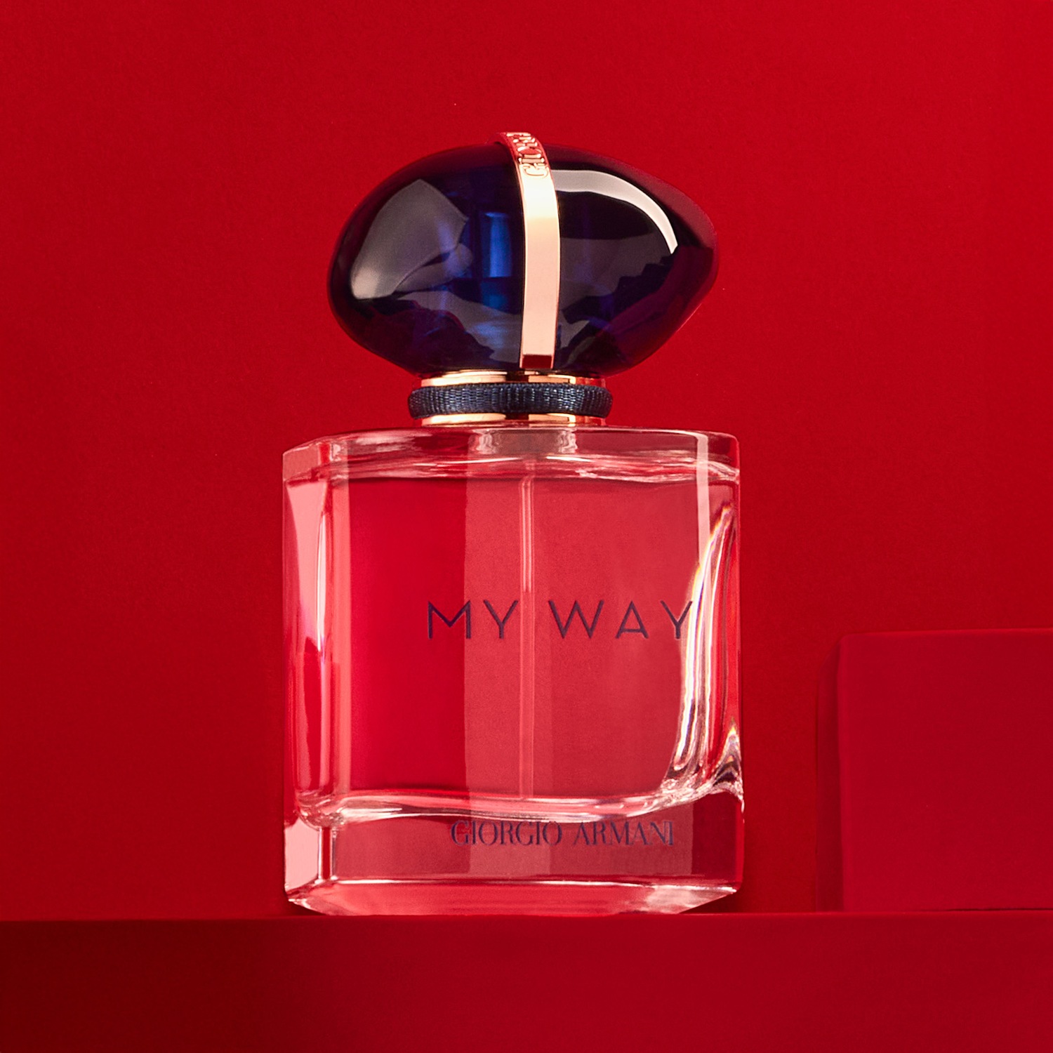 Découvrez My Way de Giorgio Armani, un parfum floral et élégant dans un flacon transparent sur fond rouge, coiffé d'un bouchon bleu nuit.