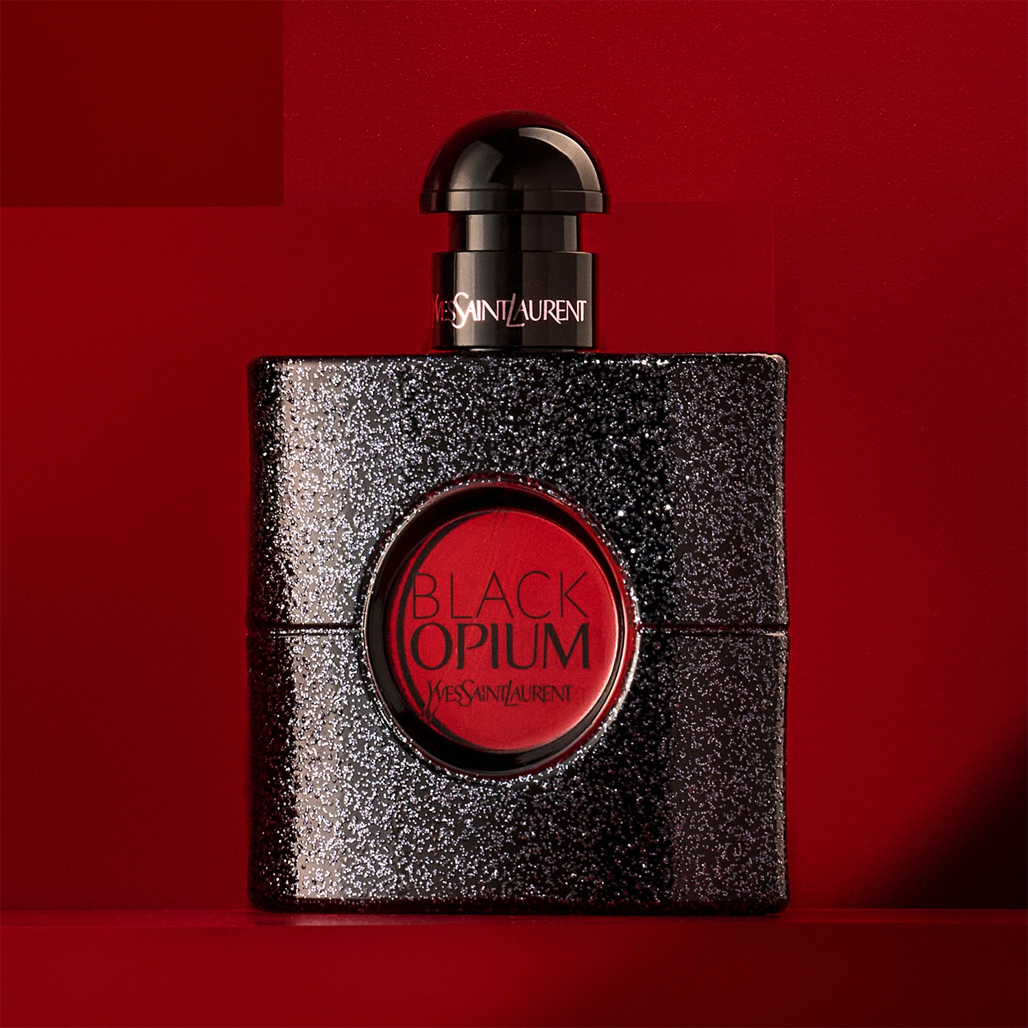 Le parfum Black Opium d'Yves Saint Laurent dans un flacon carré noir scintillant avec un logo rouge.
