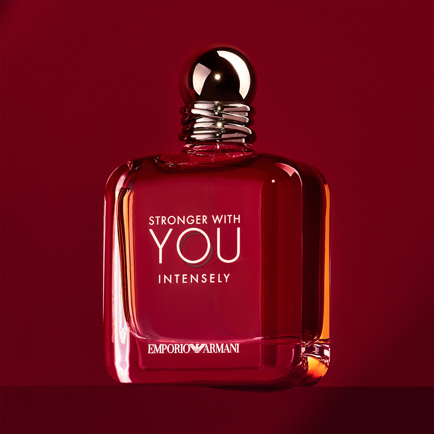 Découvrez le parfum « Stronger With You Intensely » d'Emporio Armani, présenté dans un flacon rouge rubis élégant avec un bouchon doré brillant, promesse d'une fragrance intense et captivante.