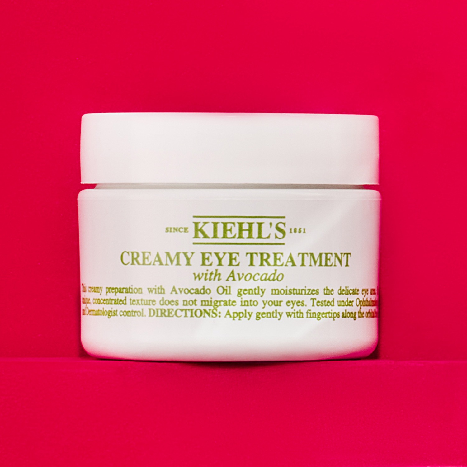 Voici le soin contour des yeux crémeux de Kiehl's, enrichi en huile d'avocat, dans un pot blanc sur un fond rose vif.