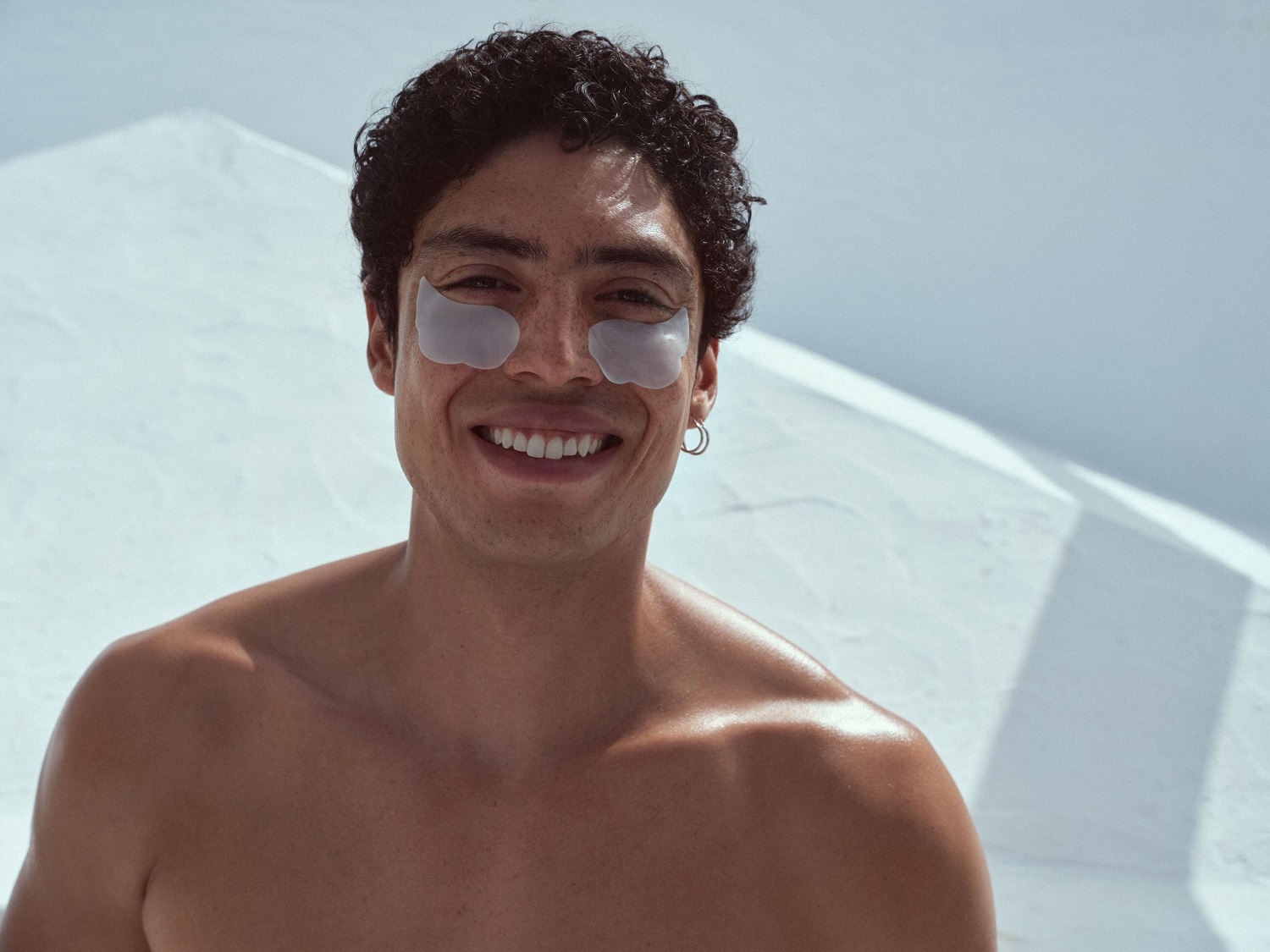 Šypsodamasis vyras su paakių kaukėmis ant veido, oda atrodo skaisti ir sudrėkinta.