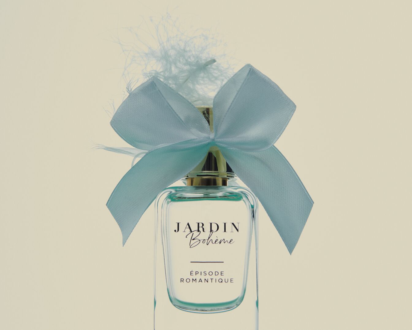 Ecco il profumo Jardin Bohème Episode Romantique, presentato in un flacone di vetro trasparente, ornato da un nastro azzurro e piume leggere.