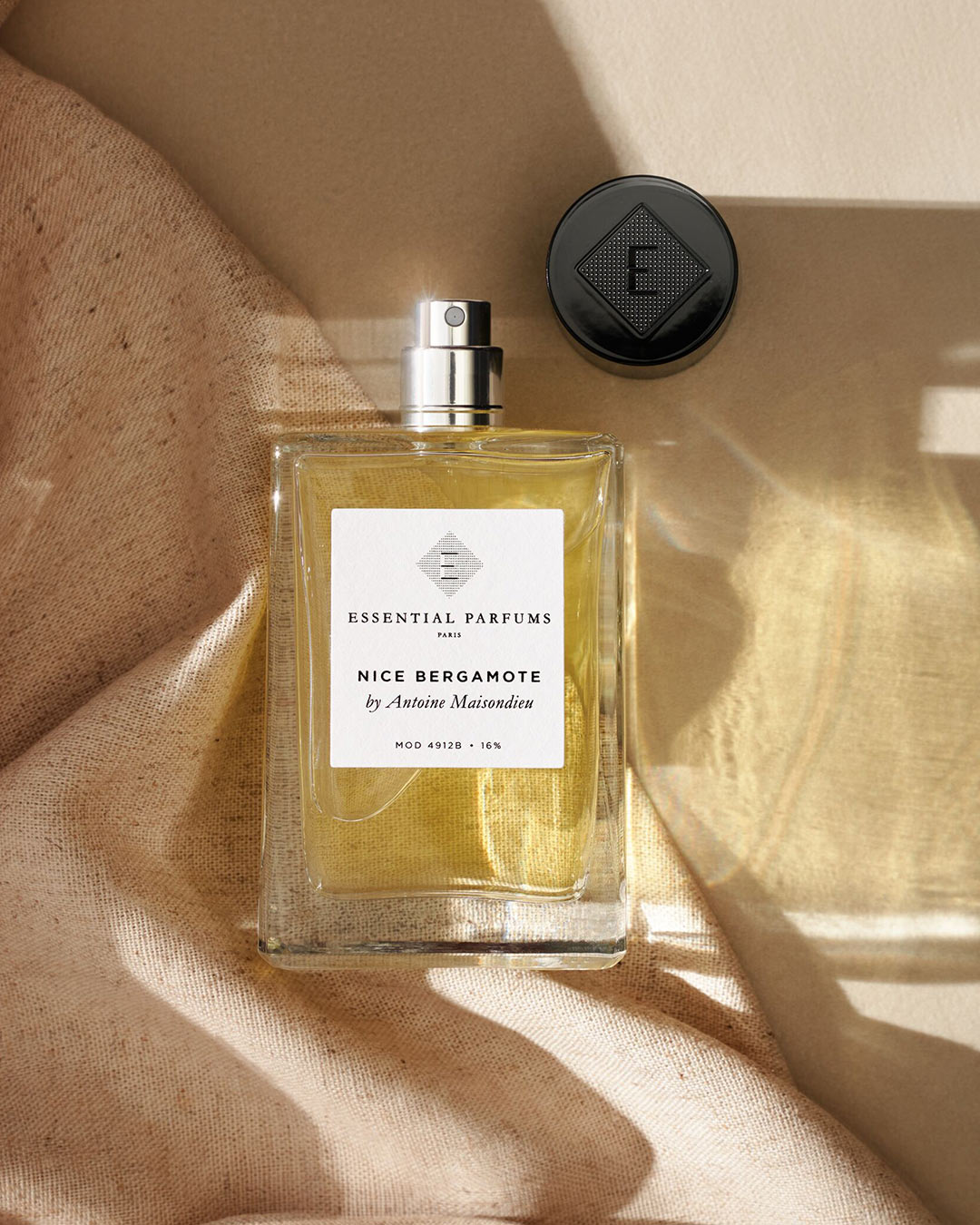 Flakon perfum Essential Parfums Nice Bergamote o pojemności 100 ml z czarną zakrętką na beżowym tle.