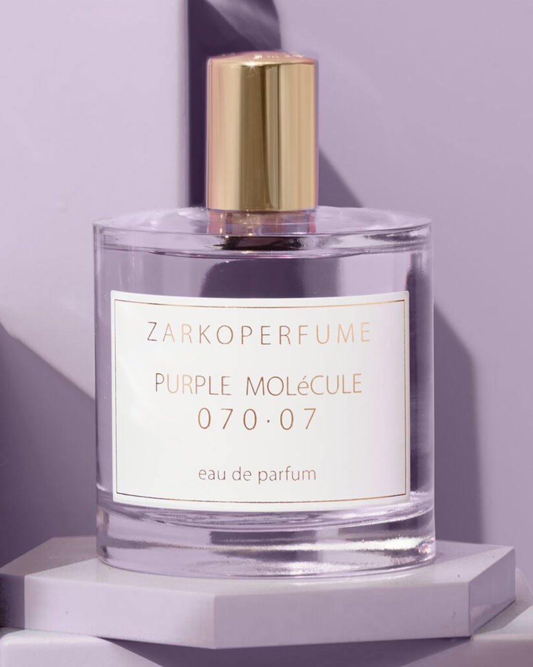 El frasco de perfume Zarkoperfume Purple Molecule 070.07 Eau de Parfum es de vidrio transparente con una etiqueta blanca y letras doradas, coronado con un tapón dorado brillante.