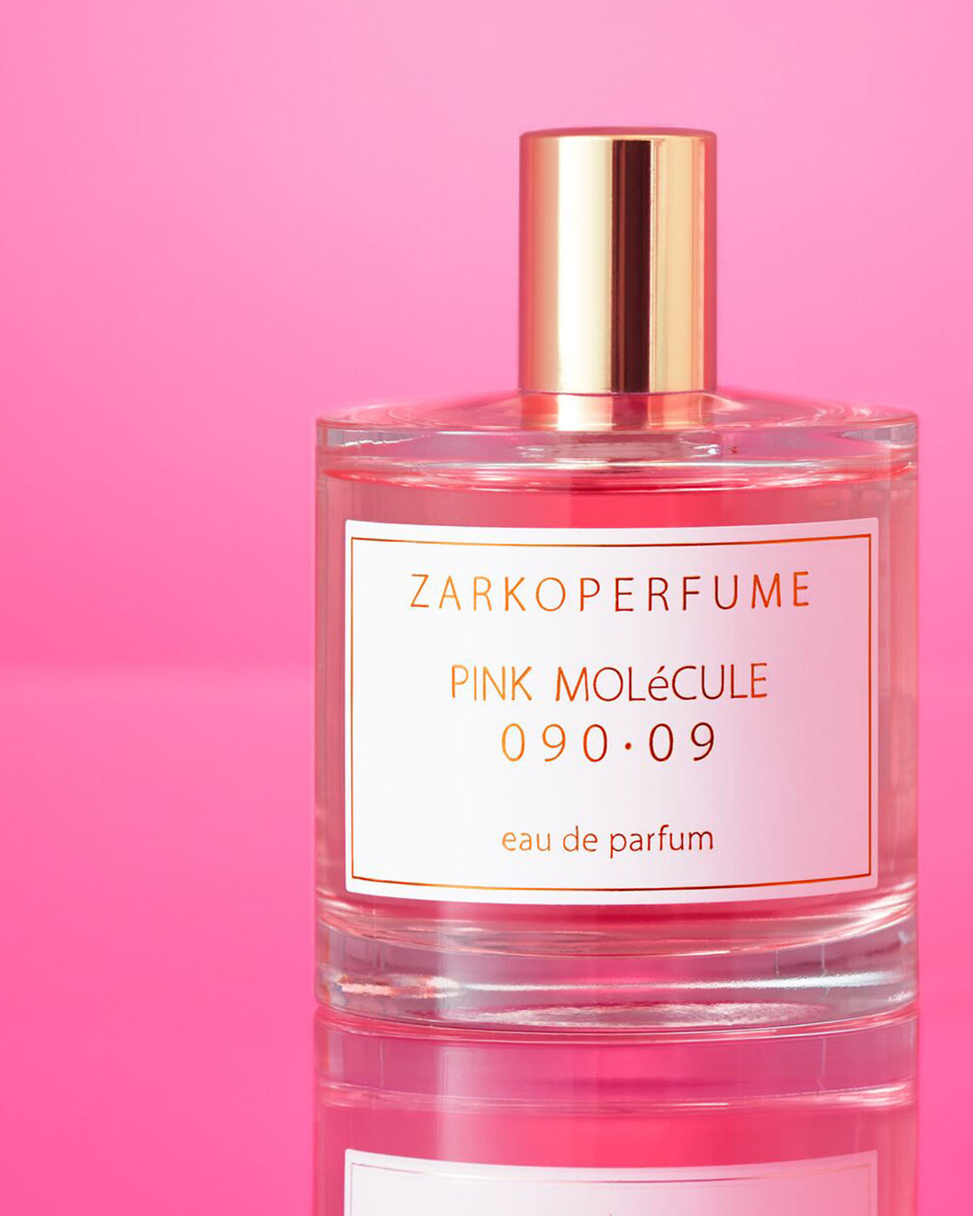 El frasco de vidrio transparente de Zarkoperfume Pink Molécule 090·09 Eau de Parfum tiene una tapa dorada brillante y una etiqueta blanca con letras doradas sobre un fondo rosa.