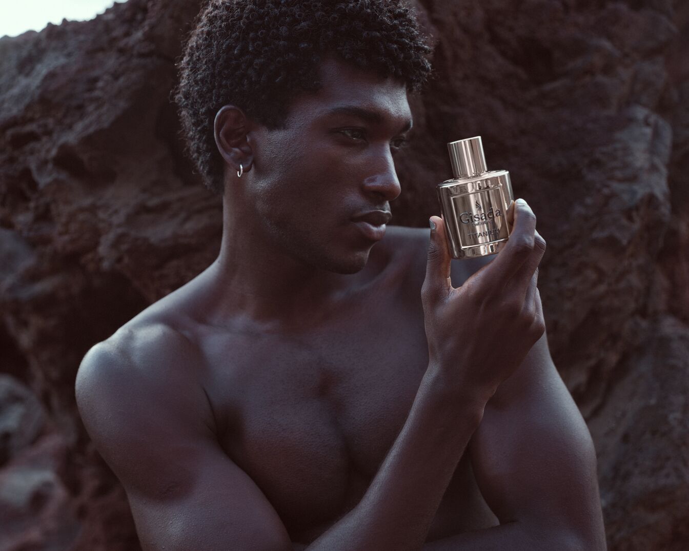 Tamsiaodis vyras be marškinių laiko rankose Gisada Titanium kvepalų buteliuką aukso spalvos pakuotėje.