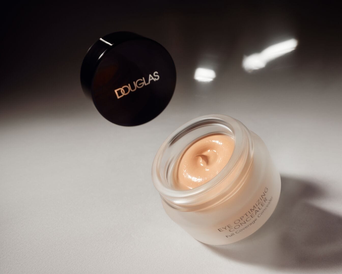 Douglas „Eye Optimizing“ maskuojamoji priemonė kreminės tekstūros, šviesiai smėlio spalvos stikliniame indelyje su juodu dangteliu, suteikia visišką padengimą.