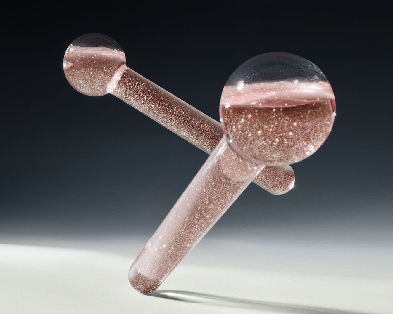 Nahaufnahme von zwei sich kreuzenden, transparenten Glasstäben, gefüllt mit einer glitzernden, rosafarbenen Flüssigkeit, die ein luxuriöses und schimmerndes Gefühl vermittelt.