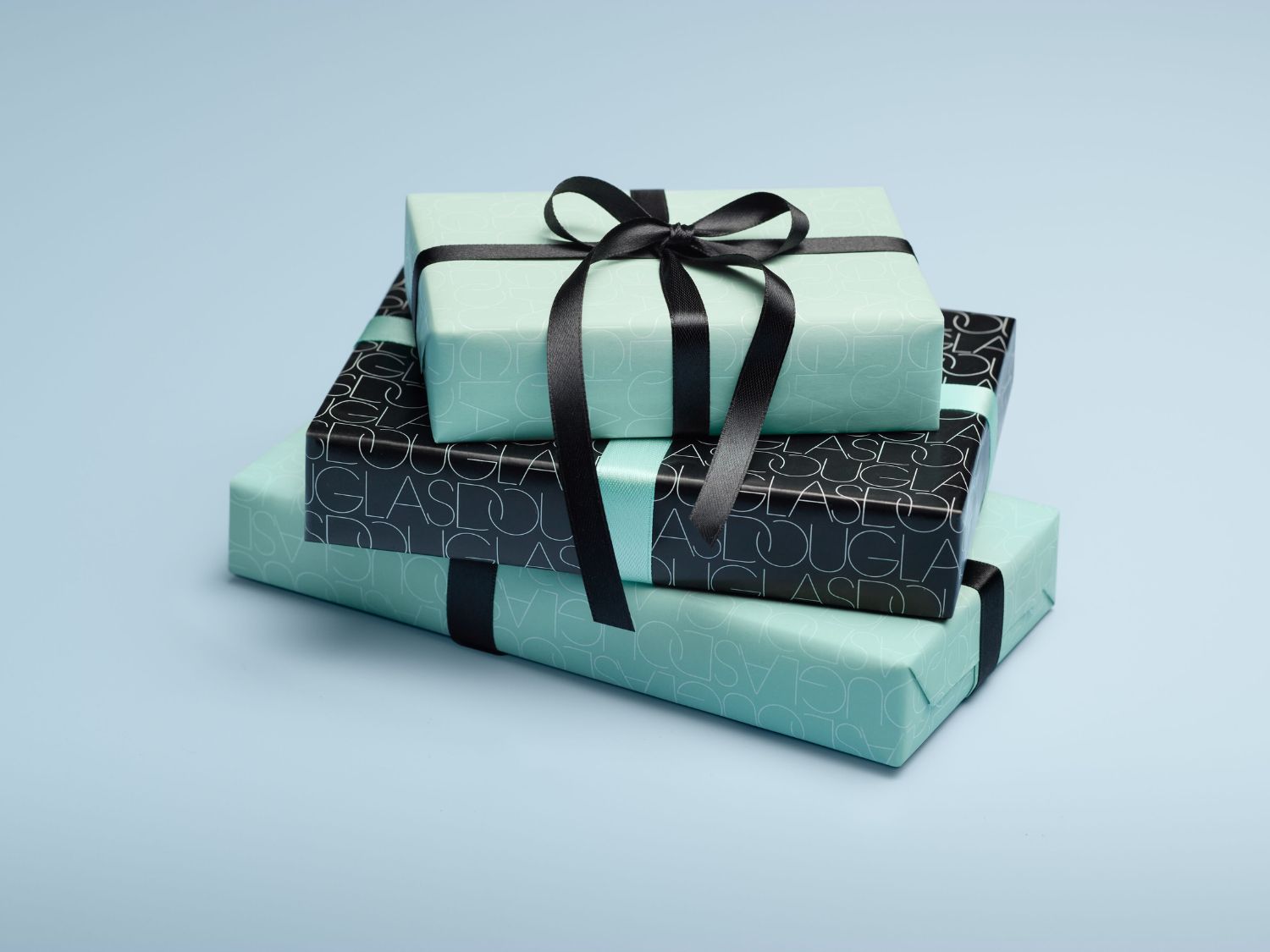 Három ajándékdoboz van egymásra rakva, a dobozok világoskék és fekete színűek, fekete szalaggal átkötve.