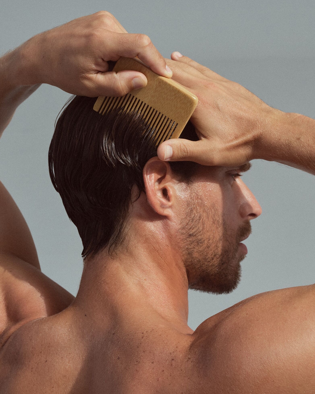 Vyras šukuojasi tamsius plaukus šviesiai rudomis medinėmis šukomis, kad sukurtų stilingą išvaizdą.