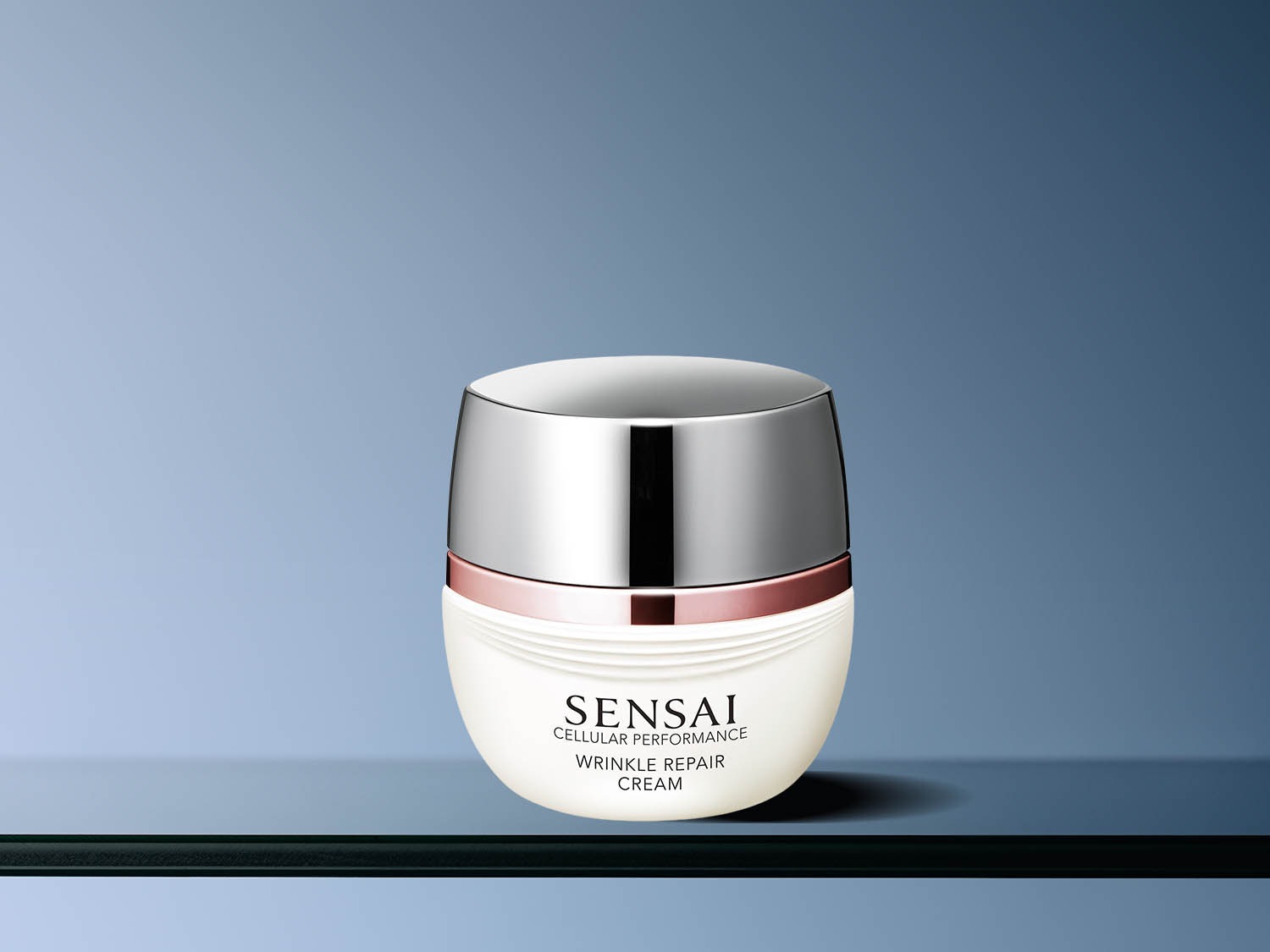 Słoik kremu Sensai Cellular Performance Wrinkle Repair Cream ma białe dno, srebrną nakrętkę i różowozłoty pasek, obiecując redukcję zmarszczek.