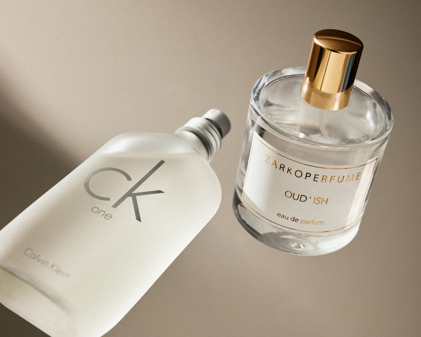 Zwei Parfümflaschen, eine CK One von Calvin Klein mit silbernem Verschluss und eine ZARKOPERFUME Oud'ish mit goldenem Verschluss, beide auf beigem Hintergrund.
