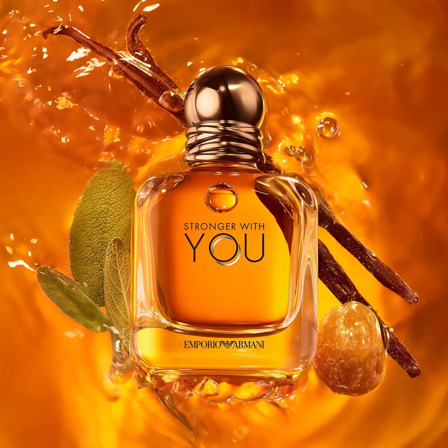Az Emporio Armani Stronger With You átlátszó üvegben, arany kupakkal, narancssárga folyadékkal, vaníliarúddal, zsályával és cukorkával körülvéve látható.