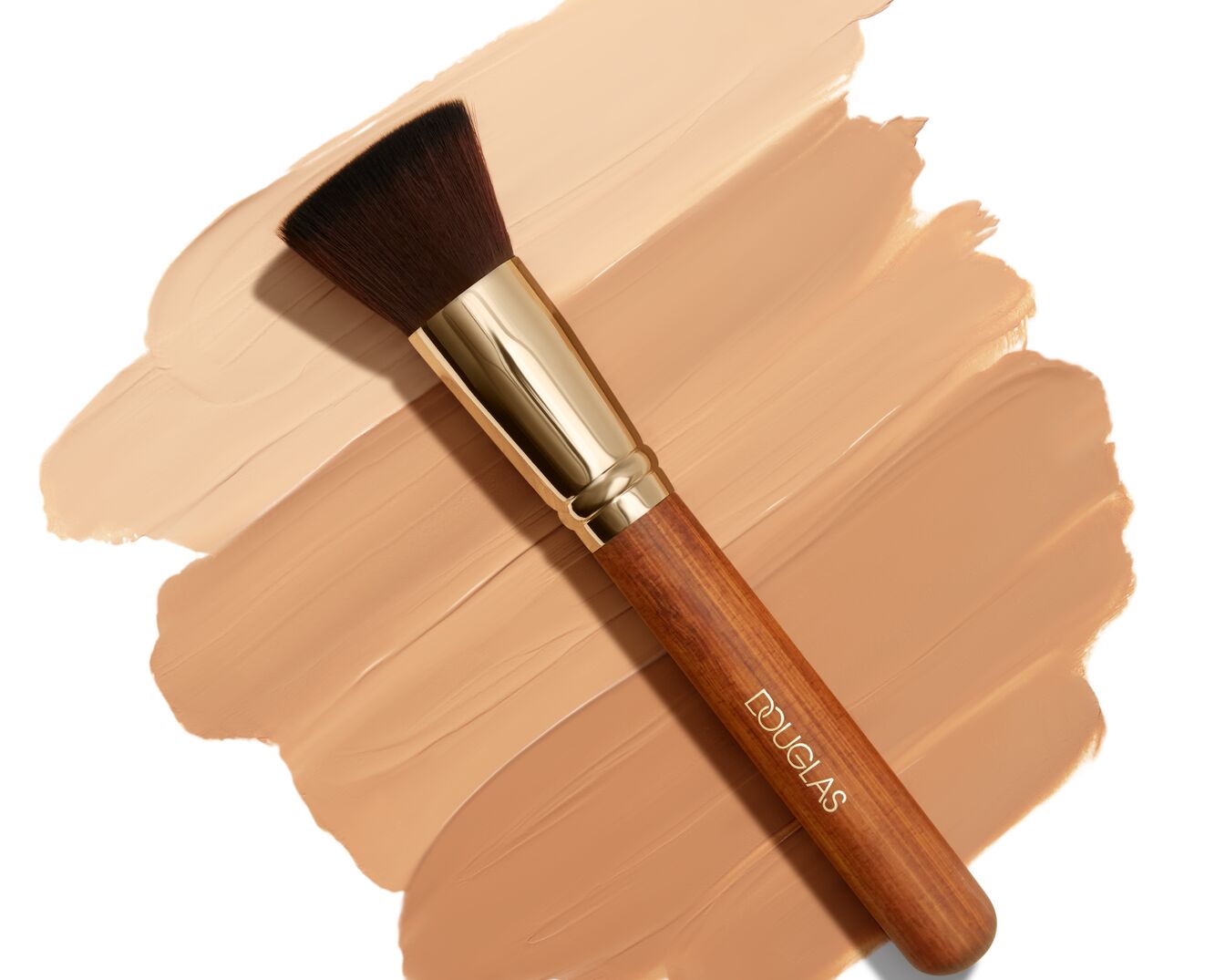 Pinsel mit Holzgriff und goldenen Akzenten liegt auf verschiedenen Farbtönen von flüssiger Foundation.