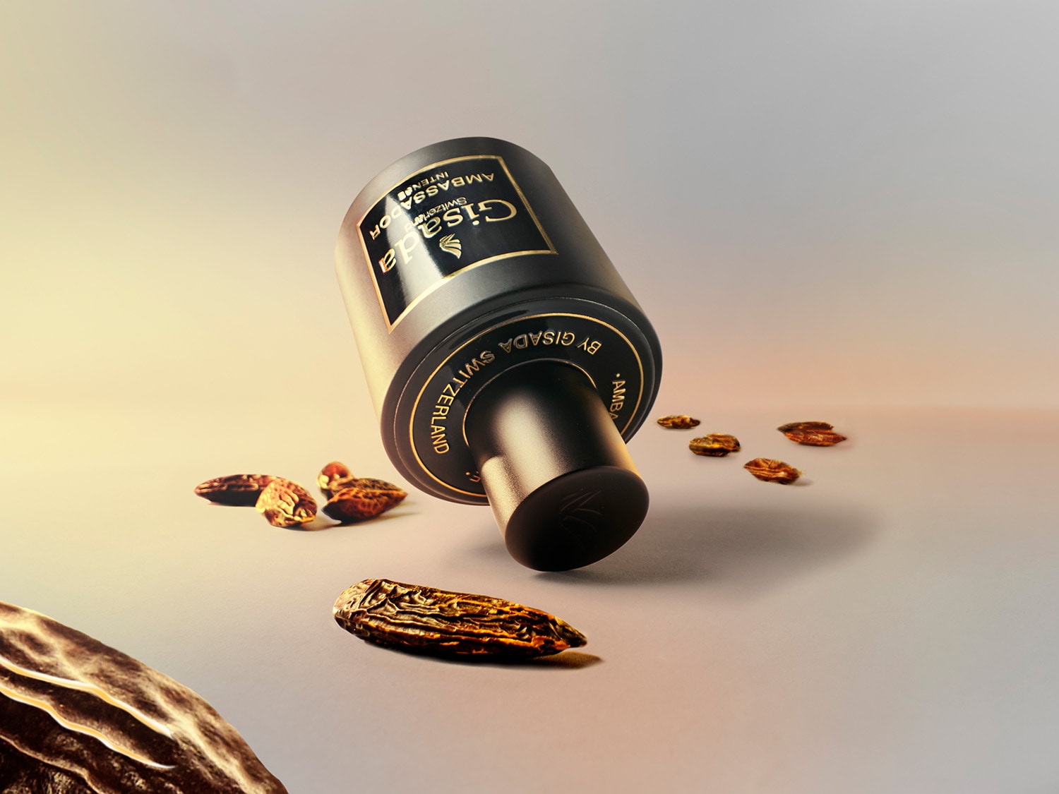 Juodas Gisada Ambassador Intense kvepalų buteliukas su auksinėmis detalėmis guli ant šono, aplinkui išsibarstę džiovinti vaisiai, pabrėžiantys aromato natūralumą.