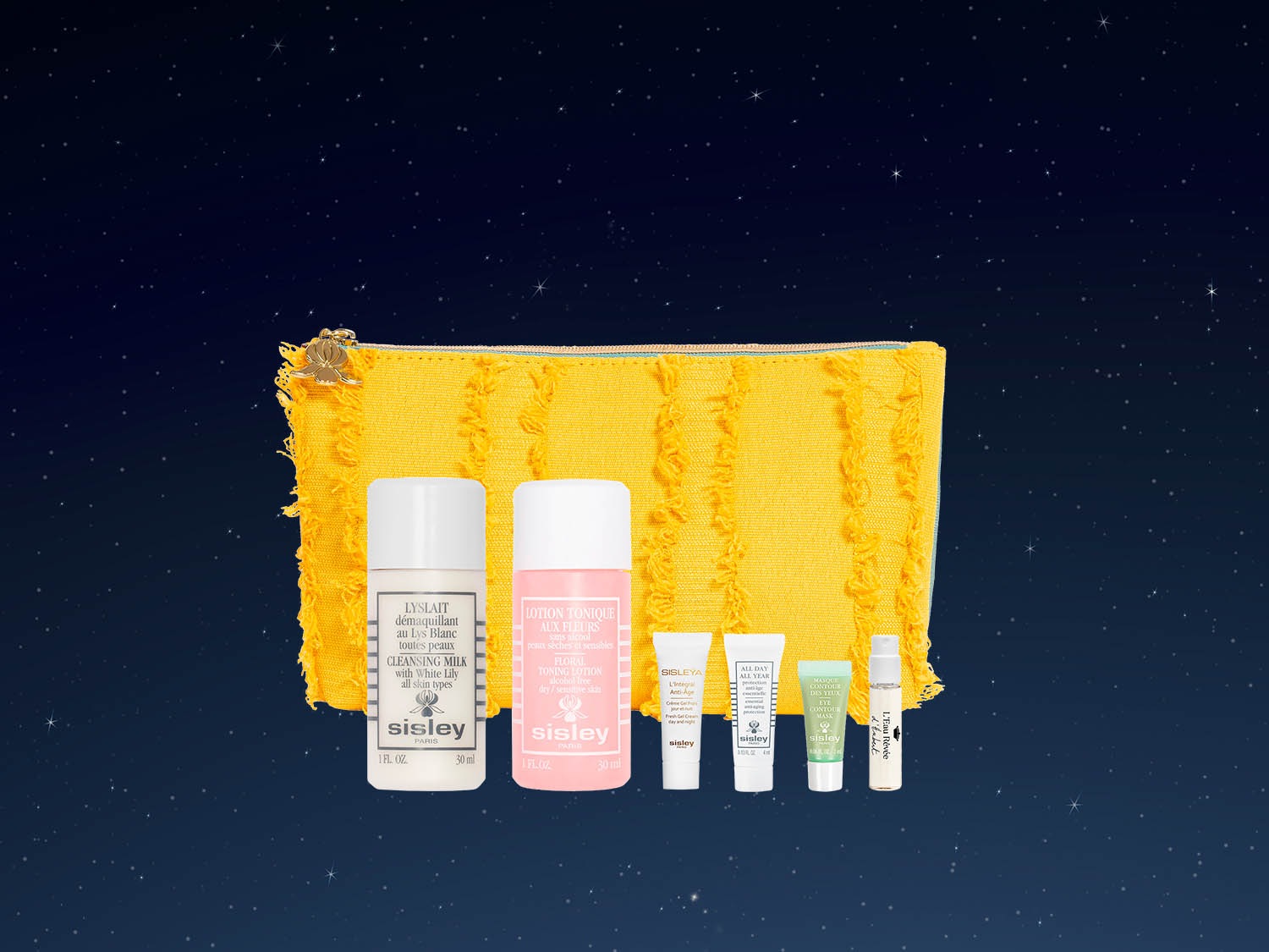 Żółta kosmetyczka Sisley z frędzlami, zawierająca mleczko do demakijażu, tonik kwiatowy i inne produkty do pielęgnacji skóry.