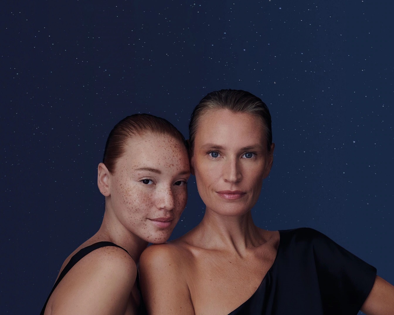 Na tle nocnego nieba z gwiazdami, dwie kobiety, młodsza z piegami i starsza, obie w czarnych sukienkach z odkrytymi ramionami, patrzą w obiektyw.